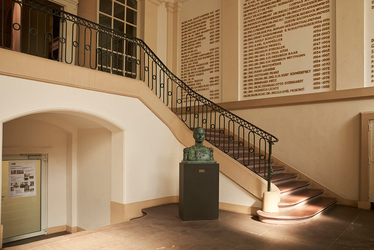 Treppenhaus mit Gedenktafel und Büste in wissenschaftlicher Einrichtung.