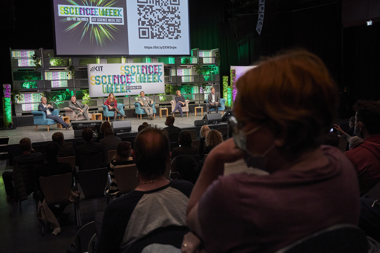 Voller Veranstaltungssaal mit Podiumsdiskussion auf der Bühne