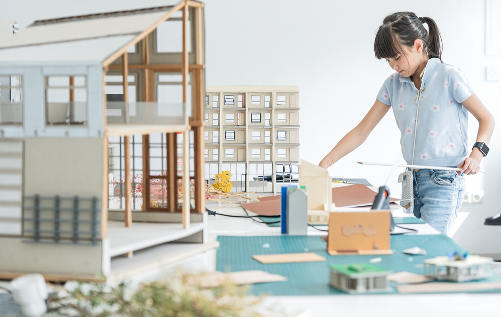 Mädchen arbeitet an Architekturmodellen auf einem Tisch.