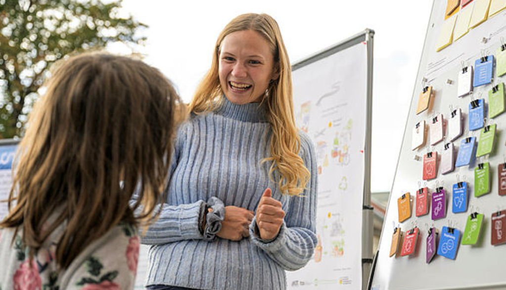 Zwei Personen diskutieren vor einem Whiteboard mit Zeichnungen; bunte Post-its an der Pinnwand.