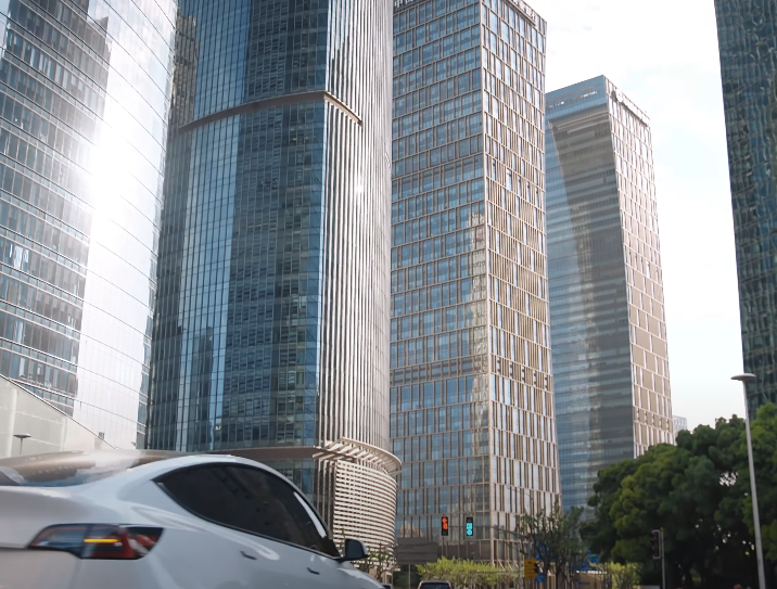 Moderne Glasfassaden von Wolkenkratzern in einer Großstadt mit vorbeifahrendem weißen Elektroauto.