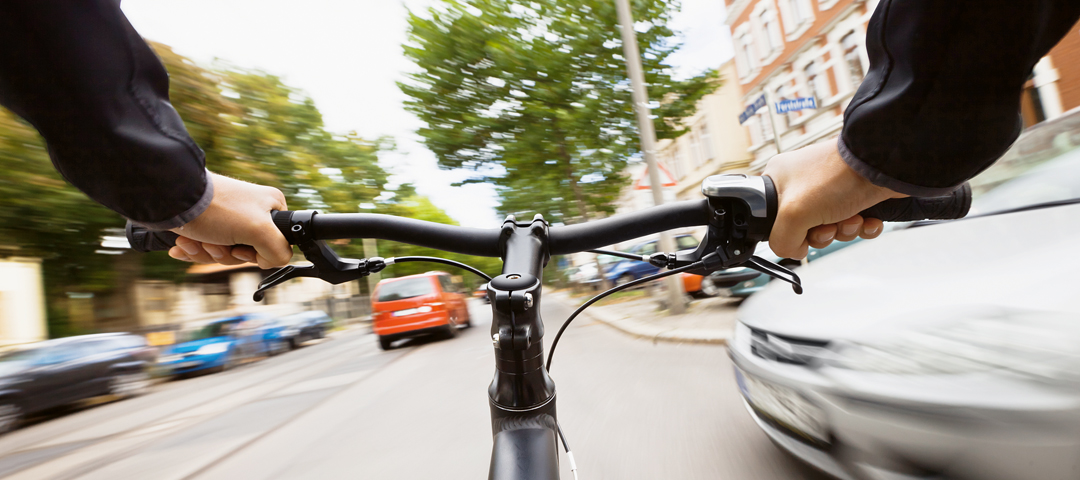 Fahrradfahrer hält Lenker und fährt schnell eine belebte Straße in der Stadt entlang.