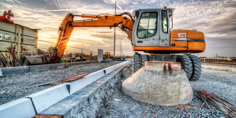 Bagger auf einer Baustelle beim Verlegen von Bordsteinen bei Sonnenuntergang.