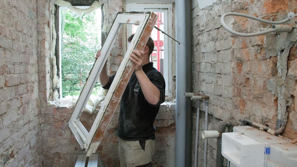 Mann entfernt altes Fensterrahmen bei Renovierung in einem Raum mit freigelegten Backsteinwänden.