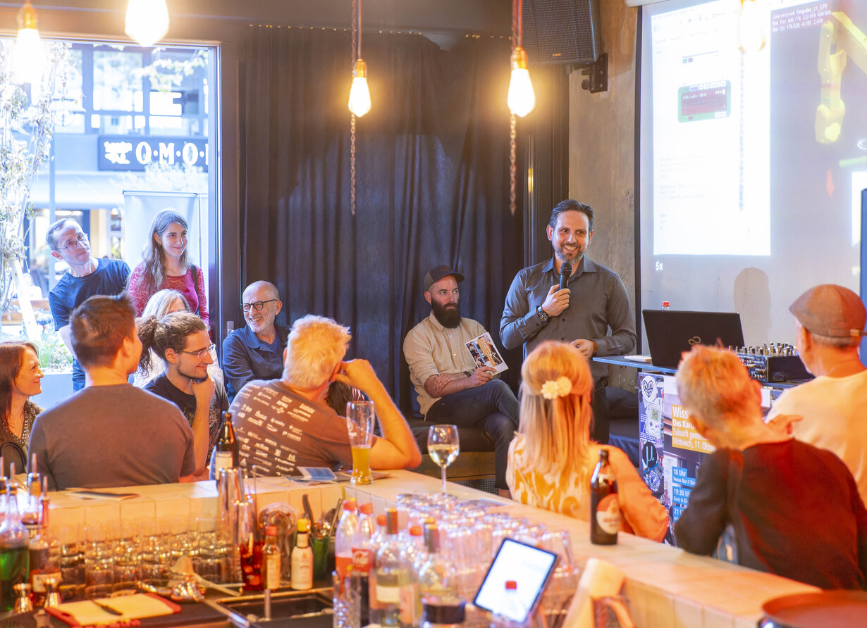 Vortrag mit Präsentation in gemütlicher Bar vor aufmerksamem Publikum.